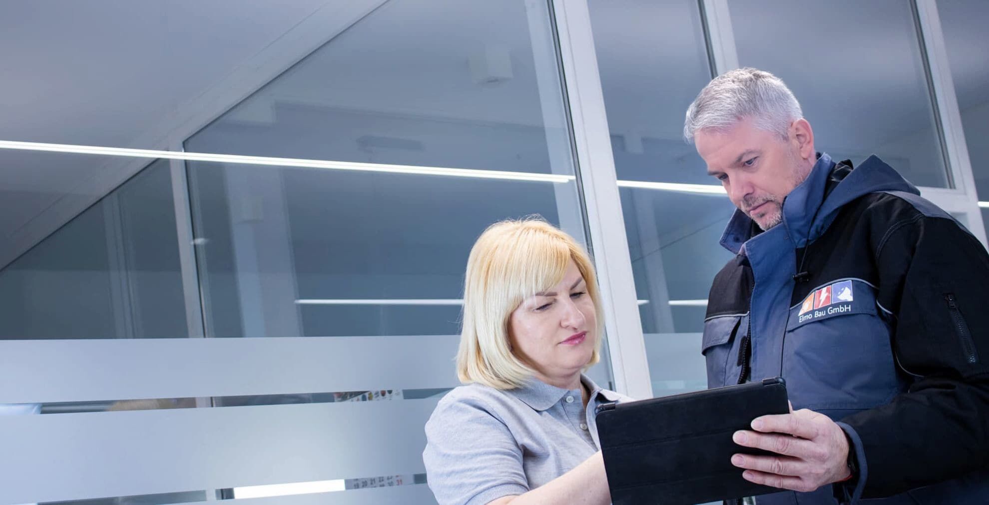 Die Geschäftsführerin zeigt mit der Hand auf ein Tablet. Neben ihr steht ein Mitarbeiter und hält ein Tablet in der Hand.