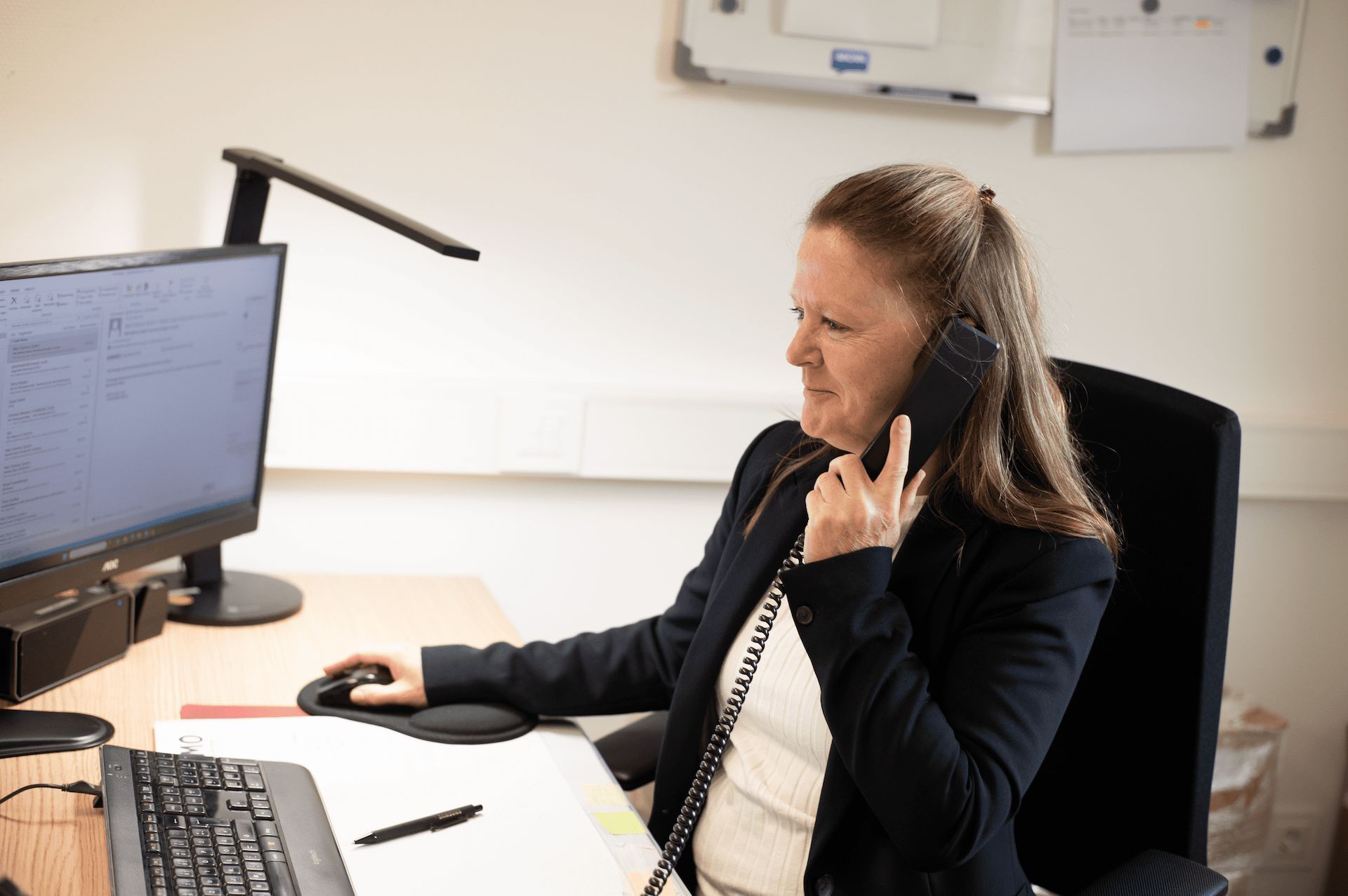 Kontaktieren Sie. Wir sind gerne für Sie da - Elmo Bau GmbH Verwaltungsmitarbeiterin der Elmo Bau GmbH beim Telefonat im Büro – serviceorientiert und professionell.